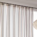Tenda leggera con righe verticali beige e marroni, montata su bastone in ferro battuto decorativo.