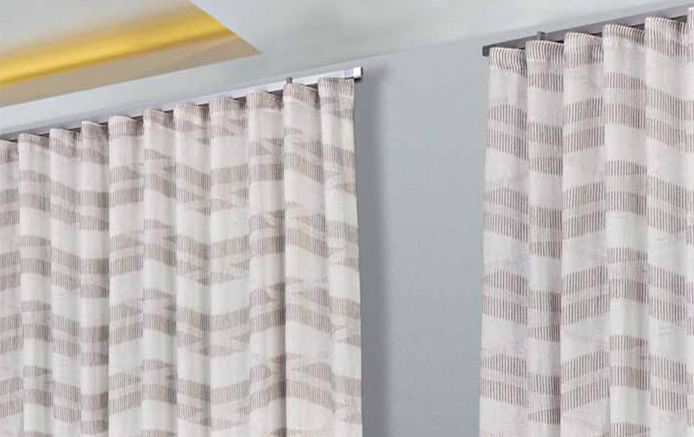 Tende a onda in tessuto geometrico beige installate su binario a soffitto in ambiente moderno