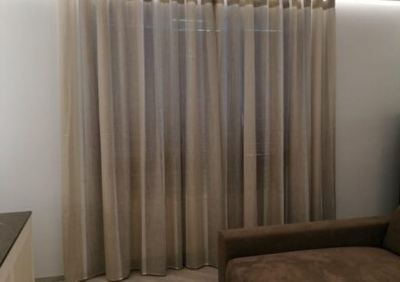 Tende a onda semitrasparenti beige davanti a finestra con illuminazione a soffitto